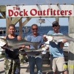 Three men proudly holding large fish at The Dock Outfitters.