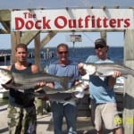Three men proudly holding large fish at The Dock Outfitters.