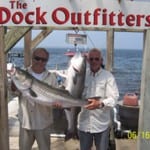 Two men proudly holding large fish at a dock outfitter.