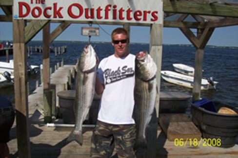 A man wearing a white shirt and a camouflage shorts while holding two huge fish