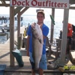 Man proudly holding a large fish at a dock outfitter.