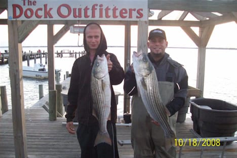 Two men wearing overall body suit while holding big fish