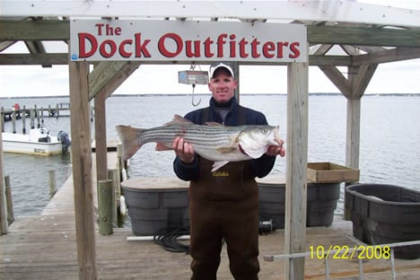 A man wearing a Navy-blue sweater and white cap while holding a big fish
