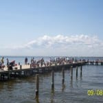 Crowded pier with people enjoying a sunny day by the water.