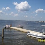 A calm waterfront with a pier extending into the water under a partly cloudy sky.