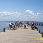 People enjoying a sunny day on a wooden pier by the water.