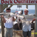 Two men wearing cap while holding big fish