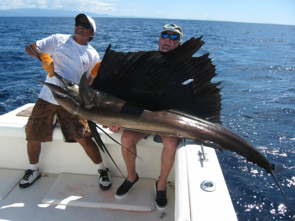 Two men on the boat and while holding a big fish