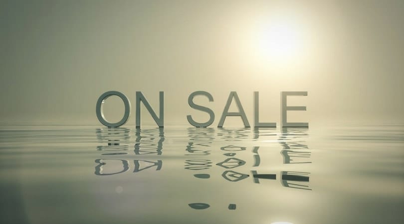 "ON SALE" sign reflected on water under soft sunlight.