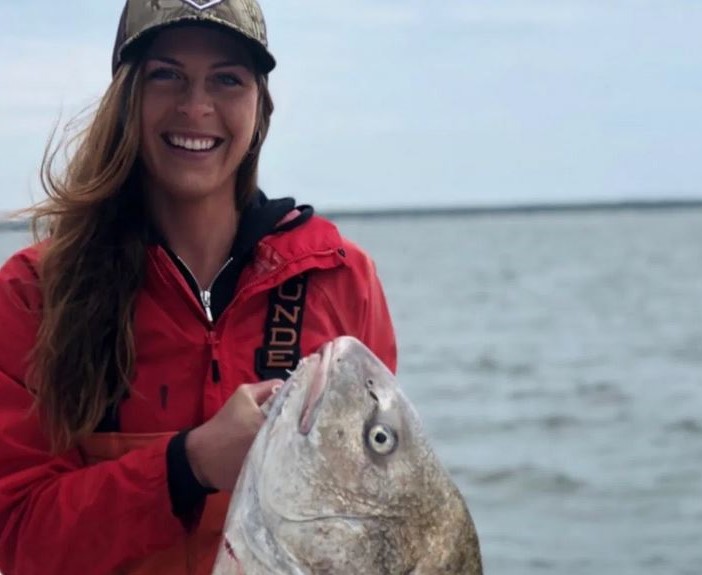 Smiling woman holding a large fish by the water.