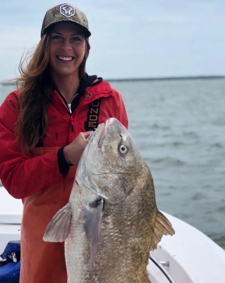 Woman proudly holding a large fish on a boat.