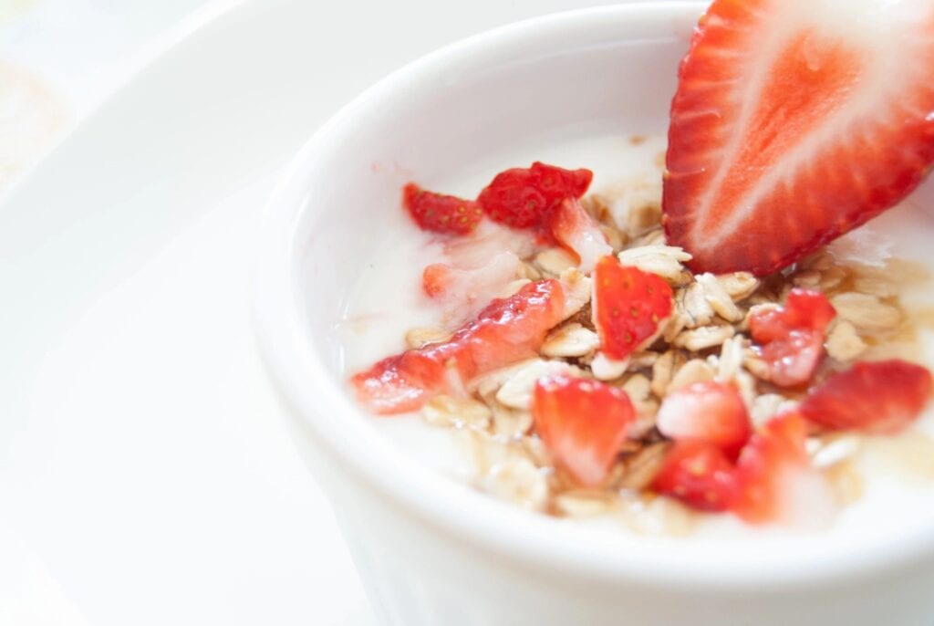 A bowl of oatmeal topped with fresh strawberries and milk.