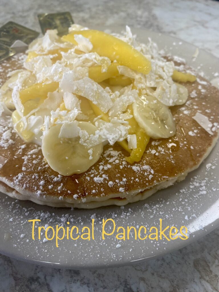 Tropical pancake topped with banana slices, pineapple chunks, and shredded coconut.
