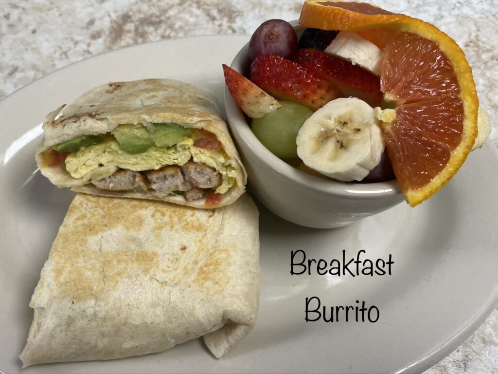 Breakfast burrito with avocado, egg, and sausage, served with fruit.